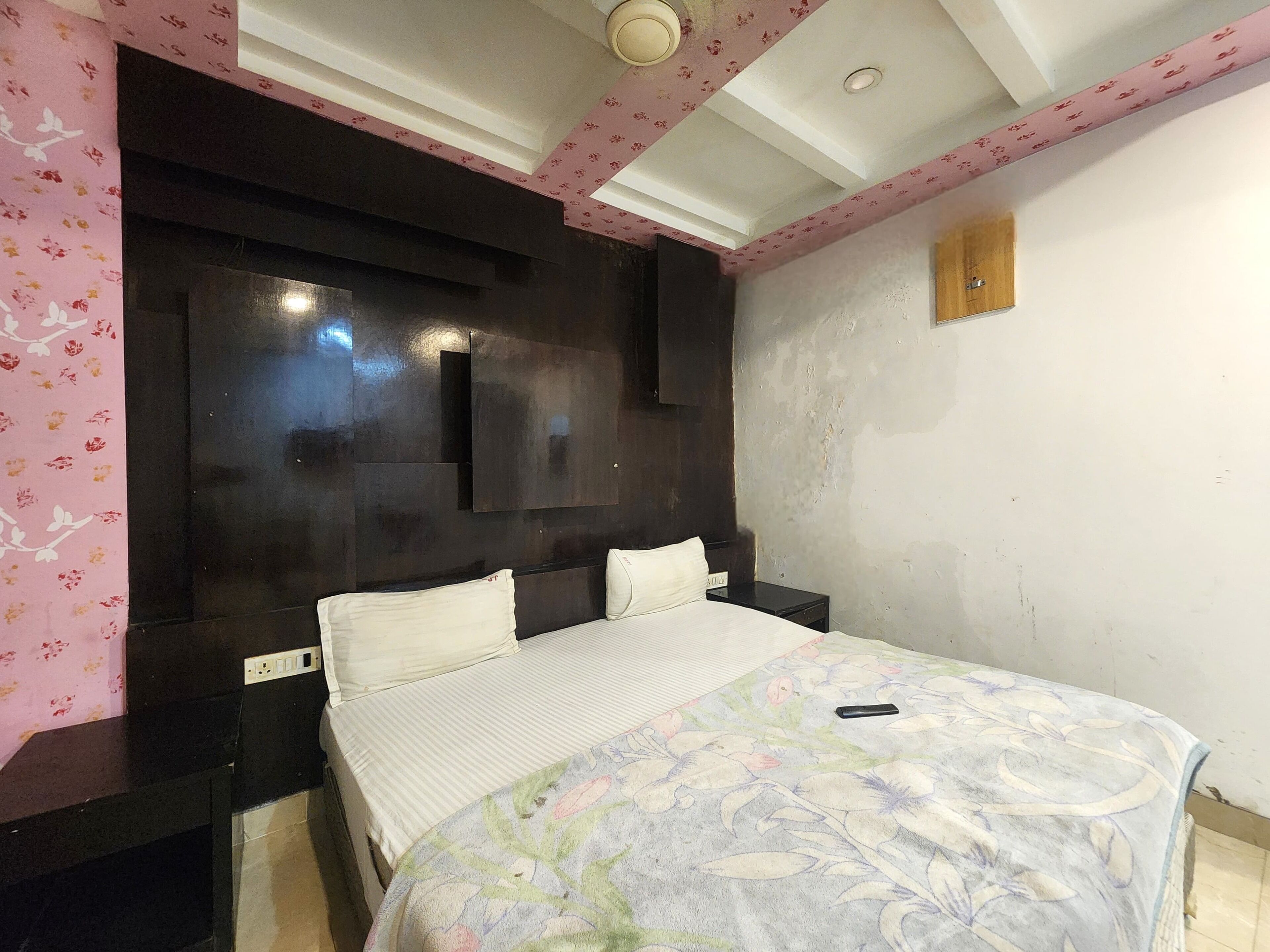 A bedroom with a bed, a nightstand, a wall-mounted TV, and a ceiling light fixture.