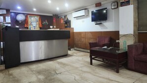 A hotel lobby with a reception desk, seating area, and a television mounted on the wall. - Hotel Florence Legacy (New Delhi)