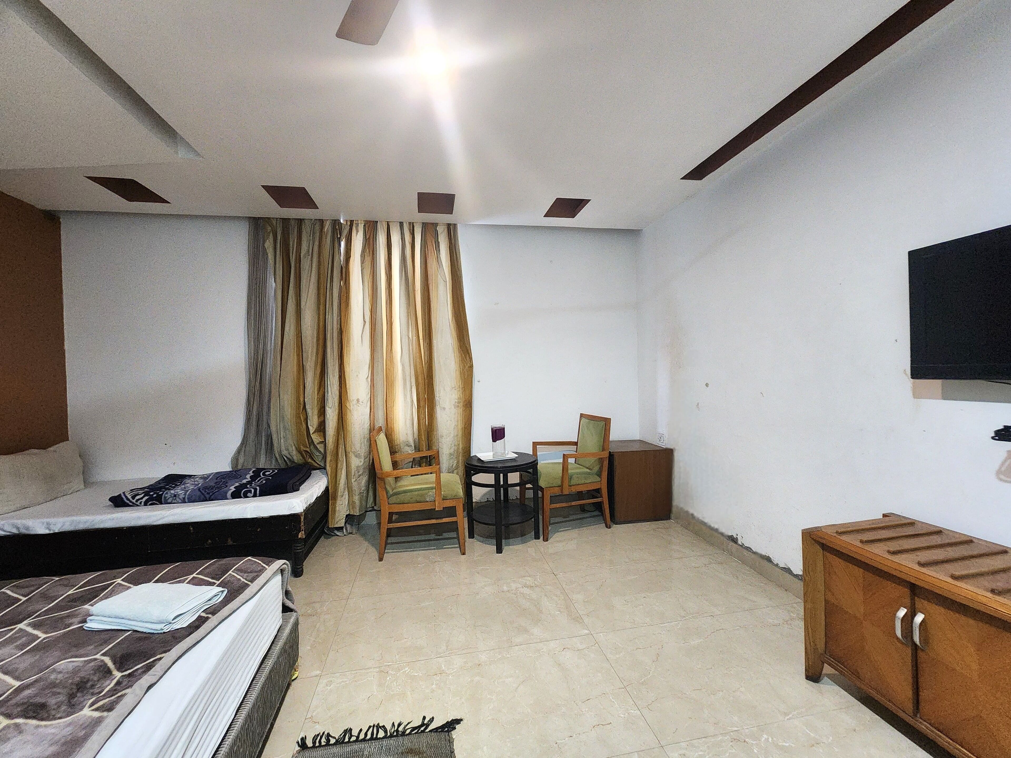 A bedroom with a bed, a chair, a small table, a cabinet, and a TV on the wall.