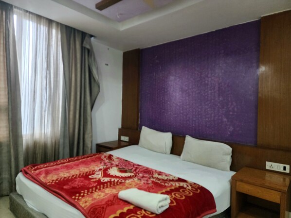 A hotel room with a bed, a nightstand, a purple accent wall, and a window with curtains. - Hotel Florence Legacy (New Delhi)