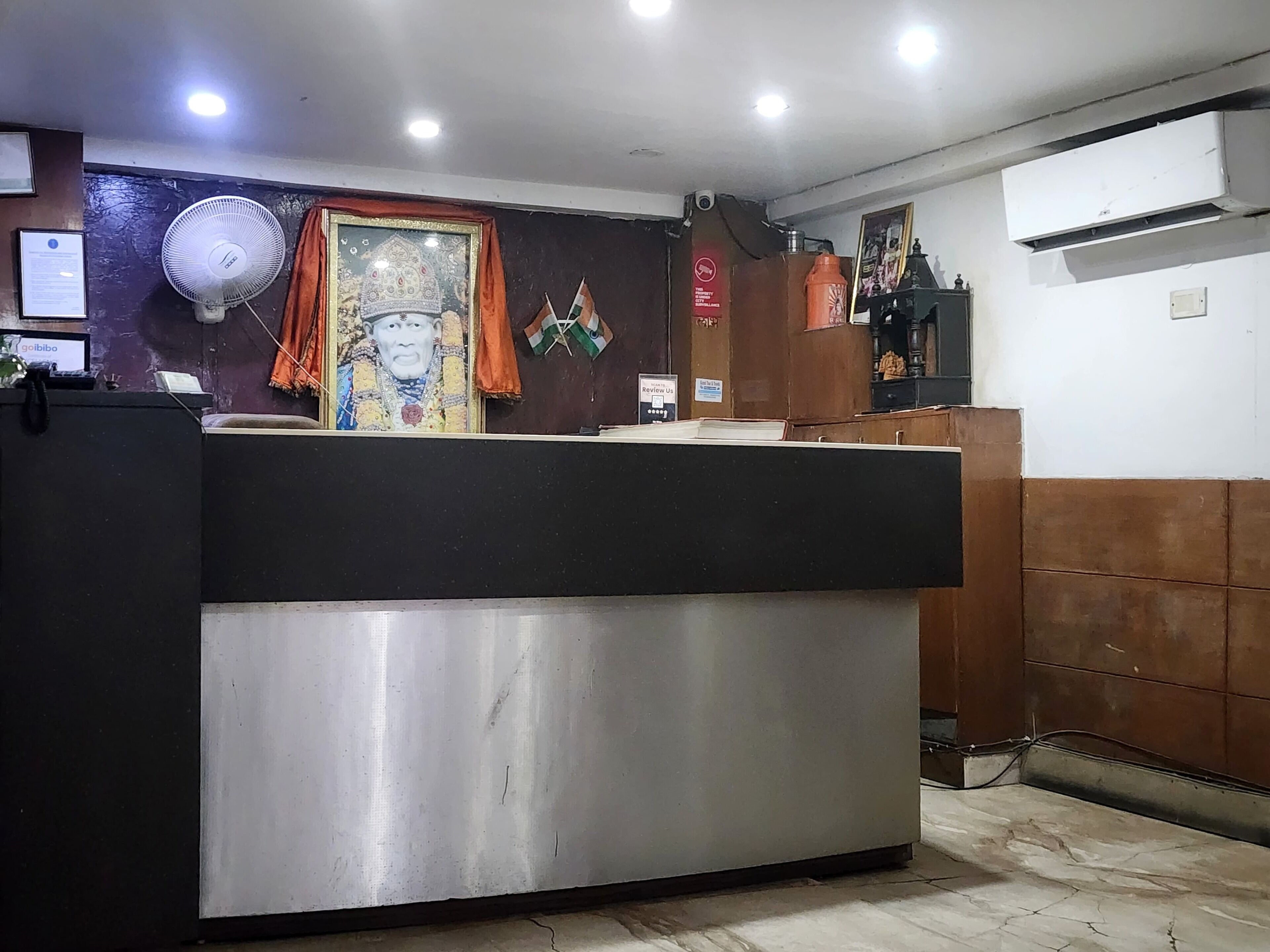 A reception area with a reception desk, a wall-mounted air conditioning unit, and a framed picture above the desk.