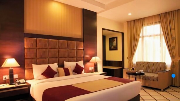 A hotel room with a large bed, two bedside tables with lamps, a sofa, and a window with curtains. - Hotel Florence Legacy (New Delhi)