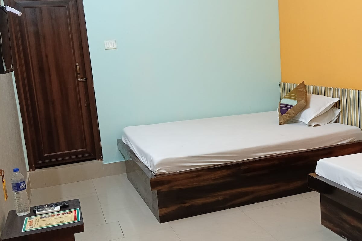 A room with a bed, a small table with a bottle and remote control, and a door.