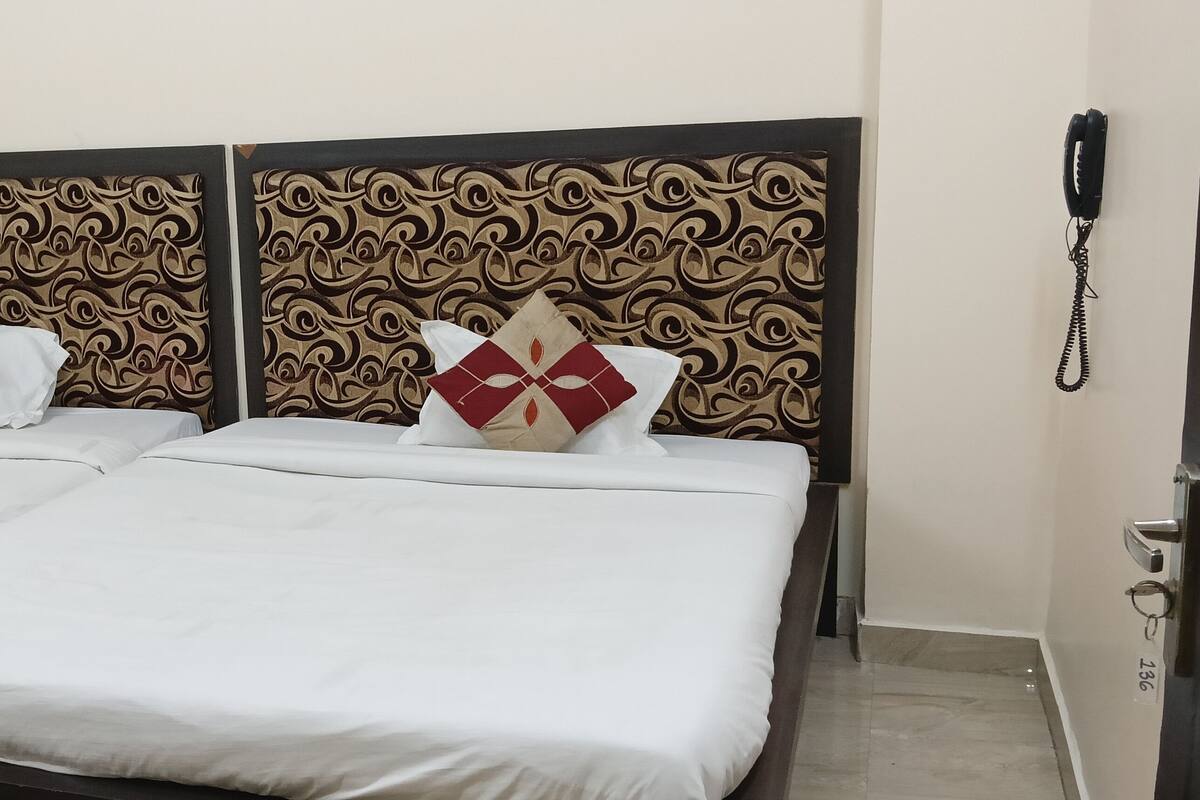 A hotel room with two beds, each with white bedding and decorative pillows. The headboards have a patterned design. A telephone is mounted on the wall to the right.