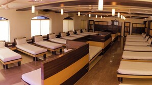 A hotel room with multiple single beds arranged in rows, a central seating area, and a television on the wall. - Sacred Stay (Guwahati)