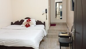 A hotel room with a bed, a desk, a chair, a phone, and a mirror. - Sacred Stay (Guwahati)