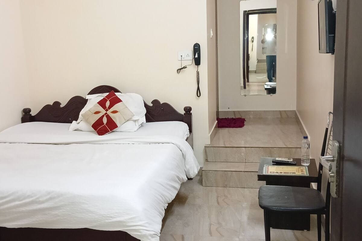 A hotel room with a bed, a desk, a chair, a phone, and a mirror.