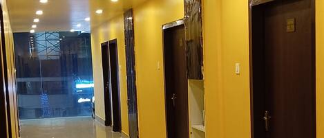A long, well-lit hallway with yellow walls and multiple doors, leading to various rooms or areas.