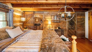 Un dormitorio de estilo cabaña de madera con una cama grande, paredes de madera, una lámpara colgante y una decoración rústica.