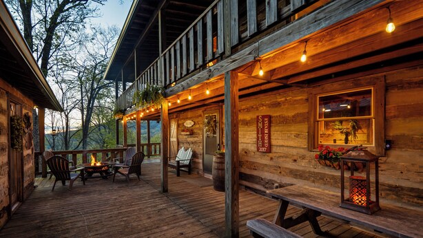 Una terraza de madera con mobiliario exterior, un hogar para fuego y luces colgantes.