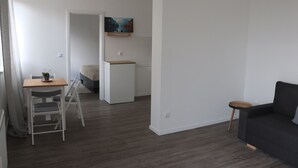 Een moderne woonkamer met een donkere bank, een kleine ronde tafel en een houten eettafel met stoelen.
