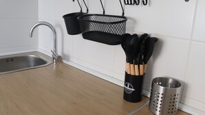Een keuken met een roestvrijstalen spoelbak, een zwart hangrek met keukengerei, en een metalen vergiet.