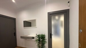 Un couloir doté d’un plancher en bois, d’une plante en pot, d’un miroir et d’une porte en verre dépoli.