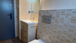 Une salle de bain moderne avec des toilettes, un lavabo et un miroir. On y trouve une porte avec une poignée et un interrupteur sur le mur.