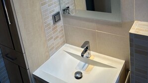 Une salle de bain moderne avec un lavabo blanc, un miroir doté d’un éclairage intégré et un mur recouvert de carreaux.