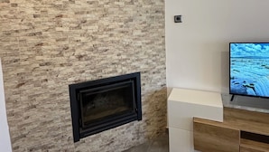 Un salon avec un mur en pierre, une cheminée, un téléviseur à écran plat et un meuble en bois.