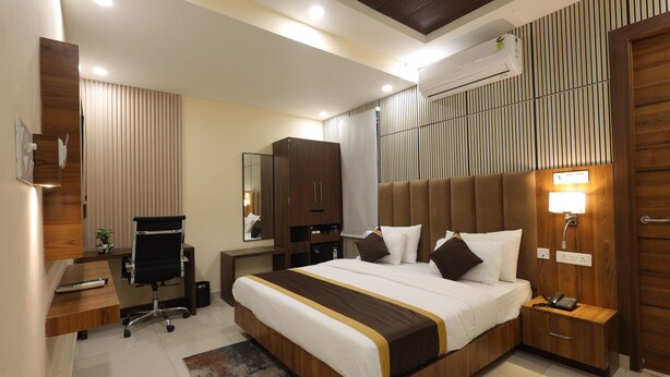 A modern hotel room with a large bed, a desk, a chair, a wardrobe, and a bedside table with a lamp. - GP Palace (Lucknow)