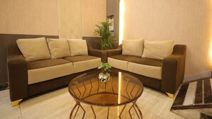 A modern living room with a brown sectional sofa, a glass coffee table, and a potted plant. - GP Palace (Lucknow)