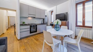 Une cuisine moderne avec des meubles blancs, une table à manger avec des chaises, un téléviseur et une fenêtre avec des rideaux.