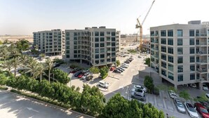 Un edificio residencial de varios pisos con un estacionamiento, rodeado de vegetación y grúas de construcción.