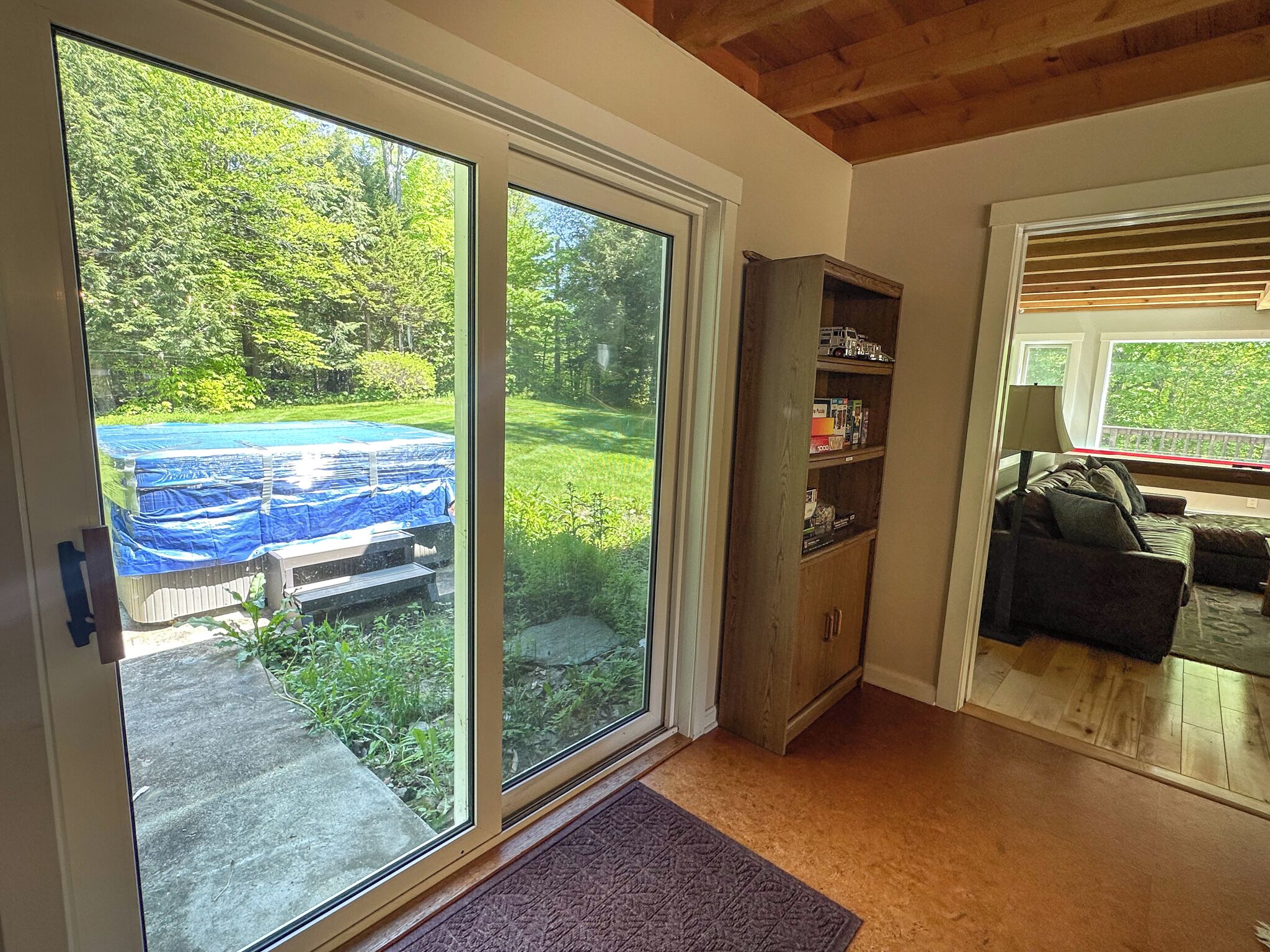 Una habitación con puerta corrediza de vidrio que da a un patio trasero con piscina cubierta y terraza de madera.