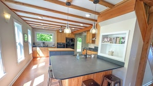 Una cocina amplia con una isla grande, vigas de madera, iluminación colgante y vistas al exterior.