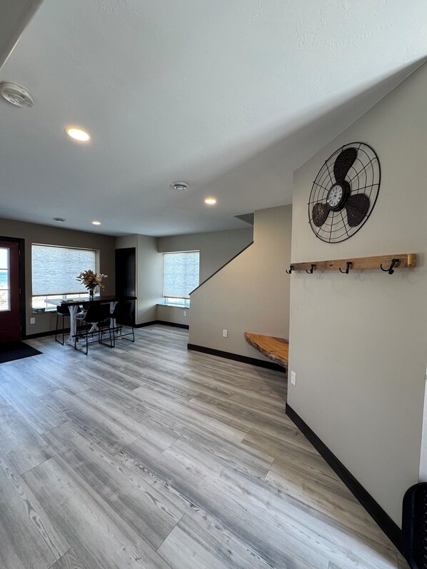 Un espacio habitable amplio con una mesa de comedor y sillas, piso de madera, ventilador de techo y una escalera que sube.