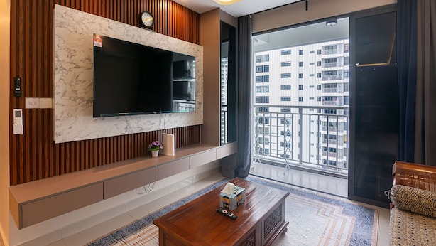 A modern living room with a large TV, wooden paneling, a sofa, a coffee table, and a view of a cityscape through a large window.