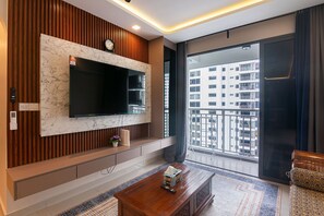 A modern living room with a large TV, wooden paneling, a sofa, a coffee table, and a view of a cityscape through a large window.