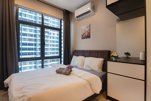 A hotel room with a large window, a bed, a bedside table with a plant, and a wall-mounted air conditioner.