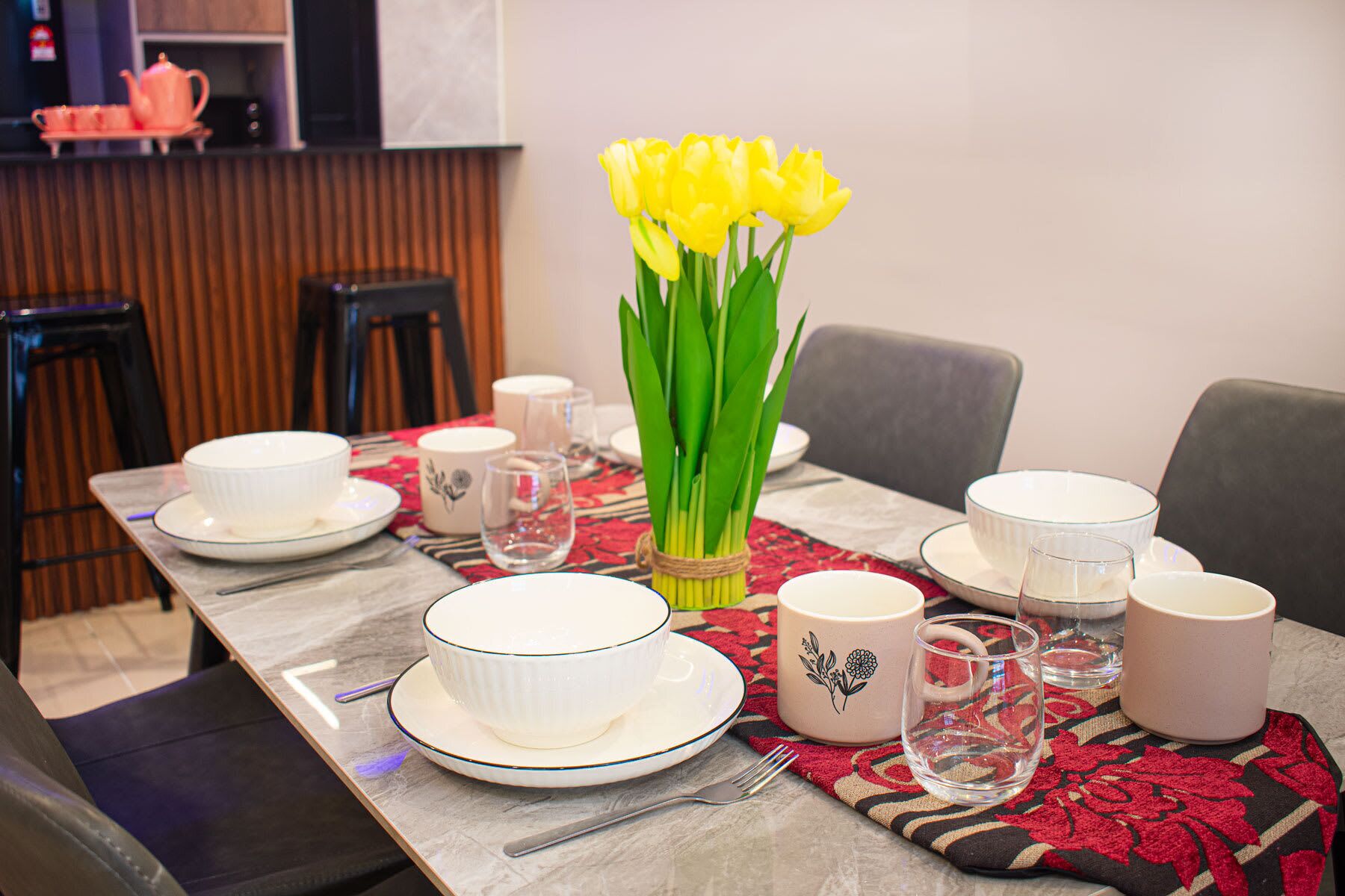 A dining table set with plates, bowls, and a vase of yellow flowers.