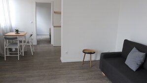 Un salon moderne avec un canapé foncé, une petite table ronde et un coin repas avec des chaises.