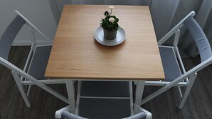 Une petite table carrée en bois, sur laquelle est posée une plante en pot, entourée de quatre chaises grises à coussin et à structure métallique.