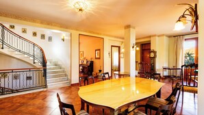 Un comedor amplio con una gran mesa de madera y sillas, una escalera con barandales decorativos y un reloj en la pared.