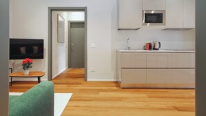 A modern kitchen with a microwave, kettle, and sink. There is a wooden floor and a green sofa in the living area. - Stylish 2BR flat in the city centre (Milan)