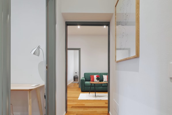 A modern living room with a green sofa, a small table with a vase, and a lamp.