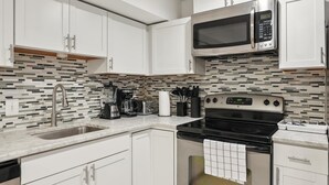 A modern kitchen with white cabinets, a stainless steel microwave, a black stove, and a tiled backsplash. - Large, 2BR/1BA with AC/TV/Internet/Laundry (Washington)