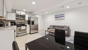 A modern kitchen with stainless steel appliances, a dining area with a black table and chairs, and a grey sofa in a living space. - Large, 2BR/1BA with AC/TV/Internet/Laundry (Washington)