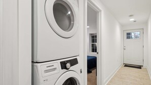 A laundry room with stacked washers and dryers, a door leading to a bedroom, and a wooden floor. - Large, 2BR/1BA with AC/TV/Internet/Laundry (Washington)