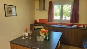 A kitchen with a dining table, two wine glasses, a bottle of wine, a fruit basket, and two Heineken beer bottles.