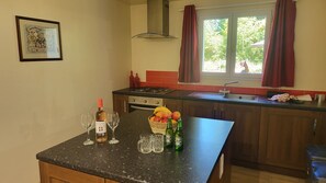 Uma cozinha com uma mesa de jantar, dois copos de vinho, uma garrafa de vinho, uma cesta de frutas e duas garrafas de cerveja Heineken.