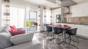 Een moderne woonkamer met een bank, een eettafel met stoelen, een keuken en uitzicht op het buitengebied.