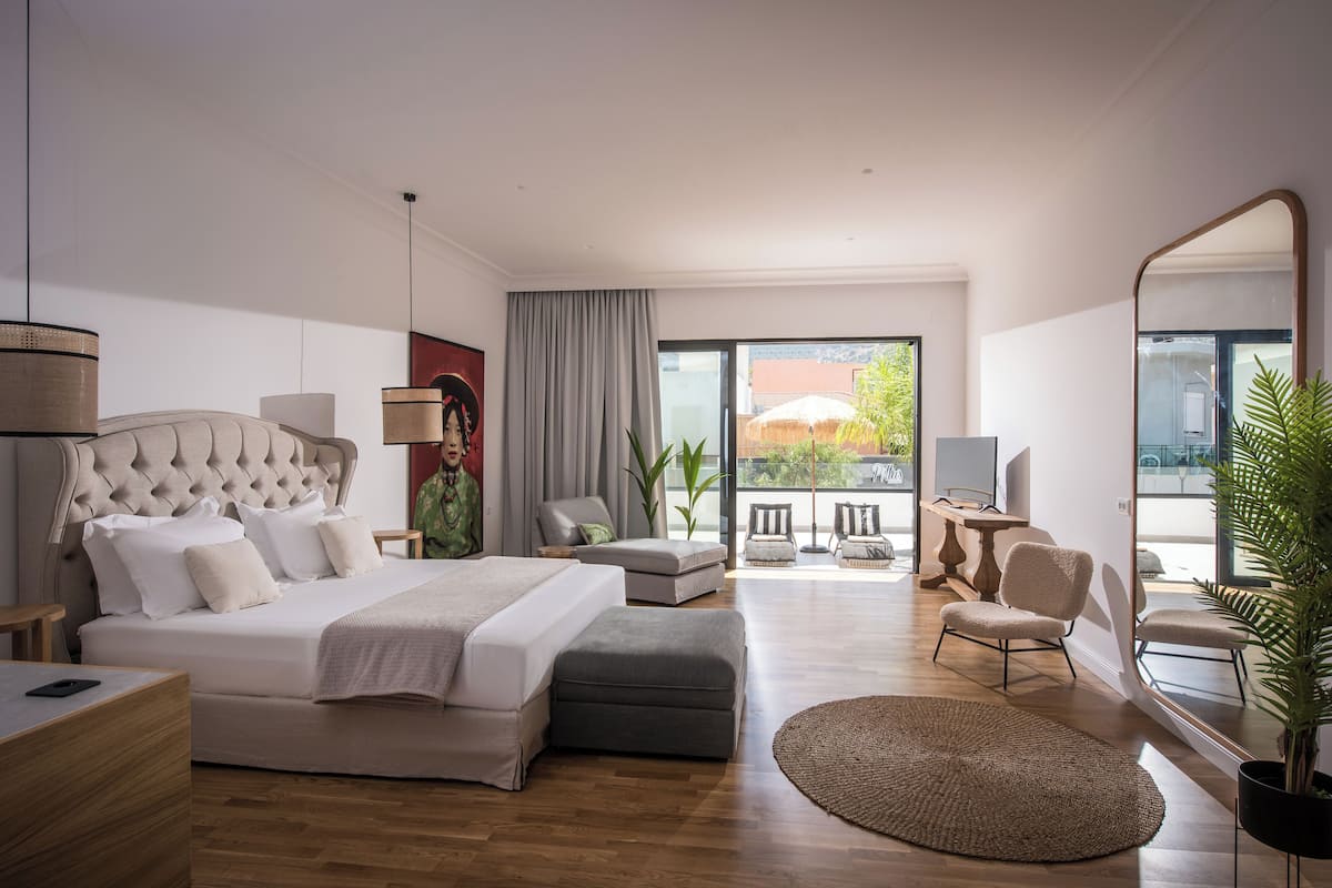 A modern hotel room with a large bed, a desk, a chair, and a balcony with a view.