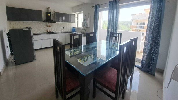 A modern kitchen with white cabinets, a black refrigerator, and a glass dining table with chairs. - Castle inn homestay (Dehradun)
