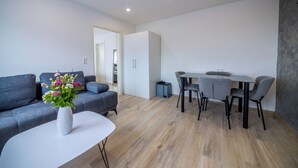 Una sala de estar moderna con un sofá gris, una mesa de centro blanca y un comedor con mesa y sillas grises.