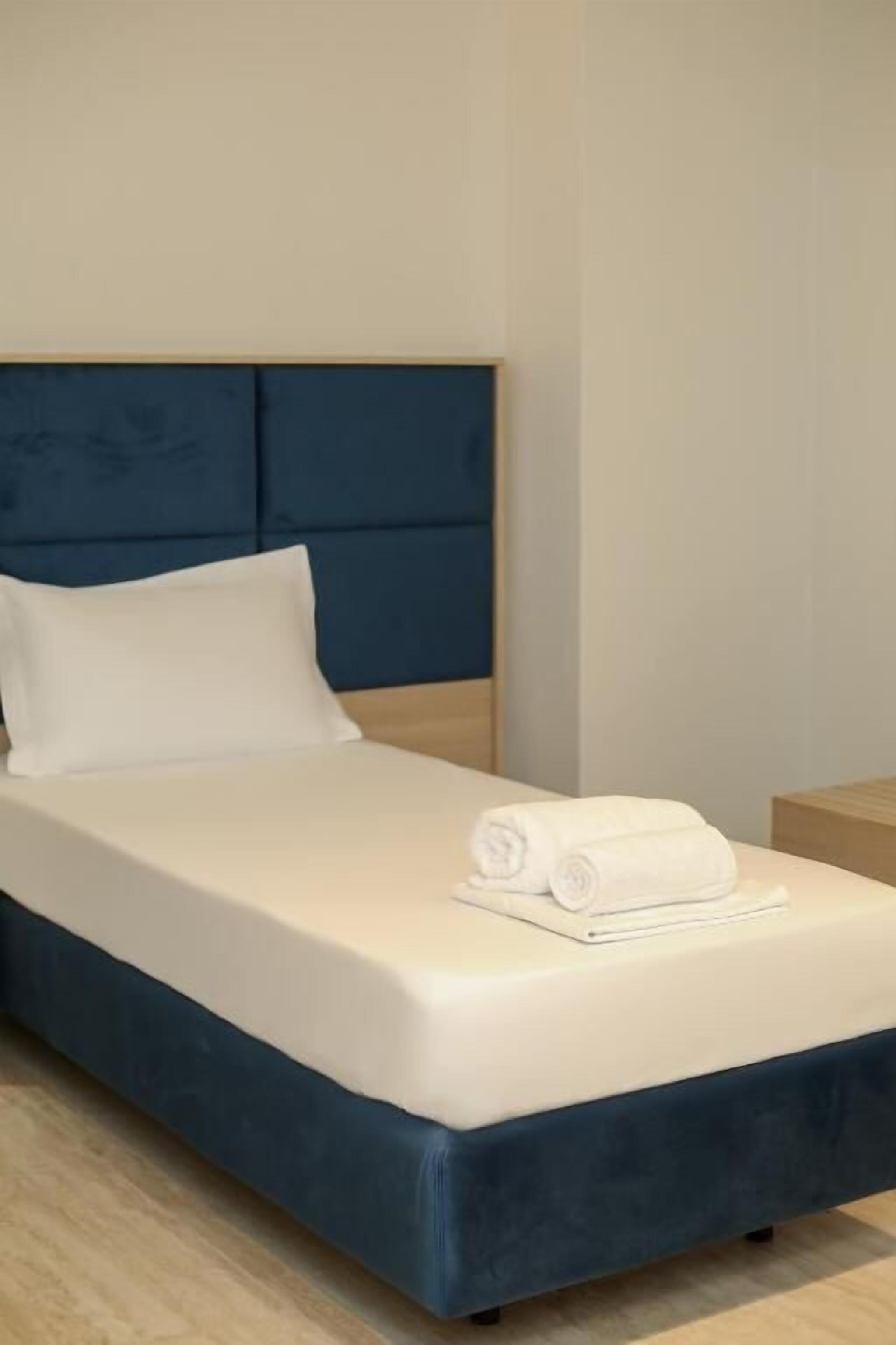 A bed with a blue headboard, white bedding, and a rolled white towel on the footboard.