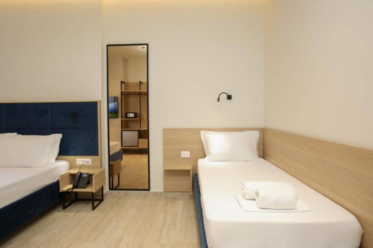 A hotel room with a bed, a bedside table with a phone, a mirror, and a wardrobe.