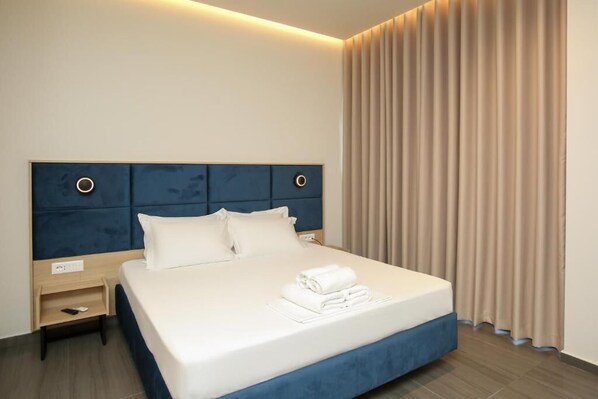 A hotel room with a large bed, a headboard with circular light fixtures, a bedside table, and a window with curtains. - ReiVal Hotel (Vlorë)
