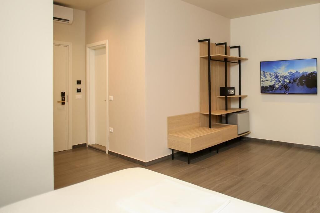 A hotel room with a bed, a wooden bench, a black shelving unit, and a framed picture on the wall.