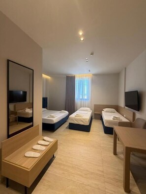 Habitación de hotel con dos camas individuales, un sofá, un televisor y una mesa de madera.